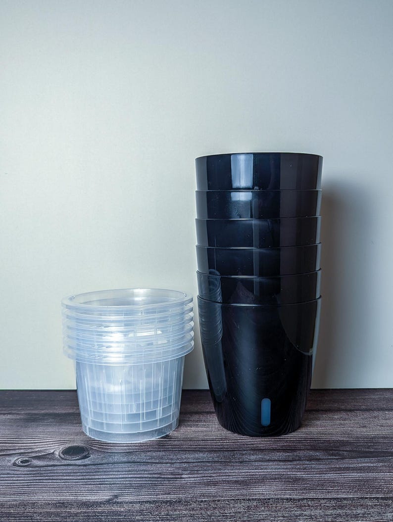 a stack of 6 black self watering pots. Black outer pot and clear inner pot sit next to each other.