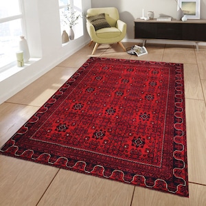 May include: A red rug with a black and white geometric pattern. The rug has a detailed border with a repeating design.