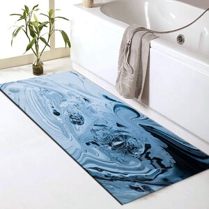 May include: A rectangular bath mat featuring a fluid, marbled pattern in shades of light blue, navy, and white. The design mimics swirling liquid paint with organic, abstract shapes and deep blue accents across the entire surface of the mat.