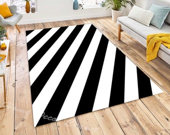 May include: A black and white striped area rug. The rug features bold, diagonal stripes, creating a striking contrast. The rug is placed on a hardwood floor in a living room setting, with a sofa, chair, and plants visible in the background.