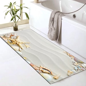 May include: A beige bath mat with a seashell and starfish design. The mat has a textured surface that resembles sand.