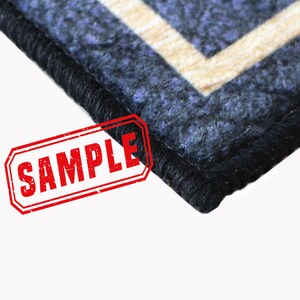Puede incluir: Primer plano de una alfombra azul y beige con estampado y borde negro. La alfombra tiene un sello "SAMPLE" en rojo.