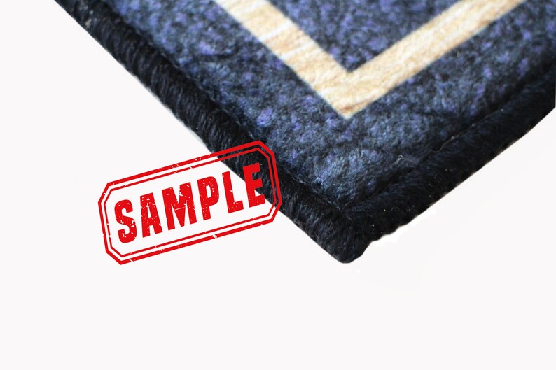 Puede incluir: Primer plano de una alfombra azul y beige con estampado y borde negro. La alfombra tiene un sello "SAMPLE" en rojo.