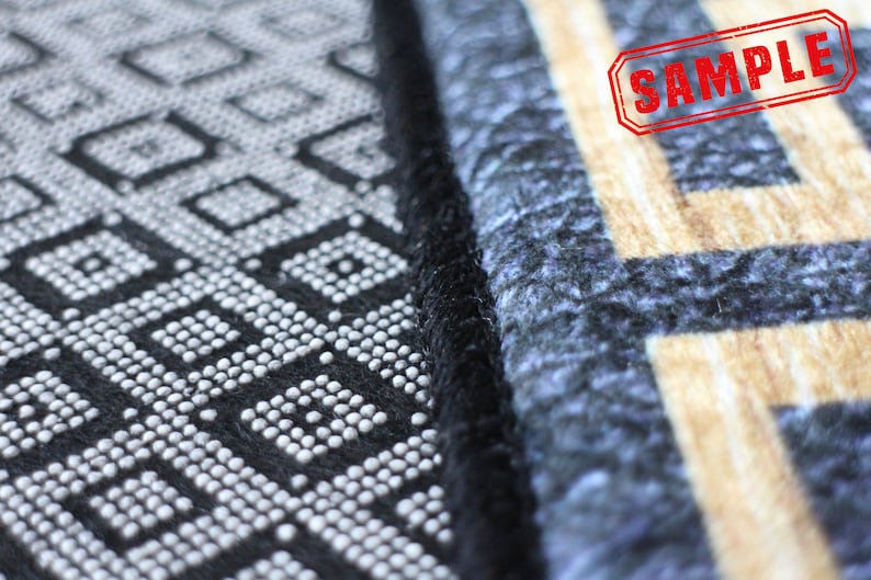 May include: Close-up of a black and white patterned rug with a black border. The rug has a geometric design with small white circles. The rug is next to a blue and beige patterned rug with a black border. The word "SAMPLE" is stamped in red on the beige rug.