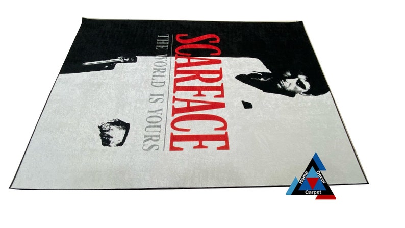 May include: A black and white rug with a picture of Al Pacino as Tony Montana from the movie Scarface. The text "Scarface" is in red and the text "The World Is Yours" is in black.