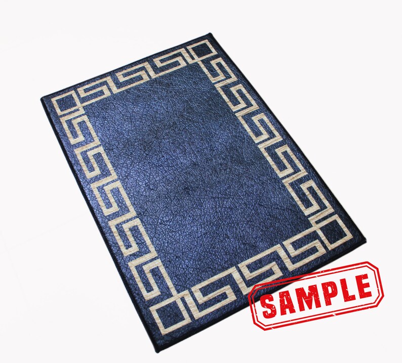 Puede incluir: Una alfombra rectangular de color azul oscuro con un borde blanco en forma de llave griega. La alfombra tiene una superficie texturizada y la palabra "SAMPLE" est&aacute; estampada en rojo en la esquina inferior derecha.