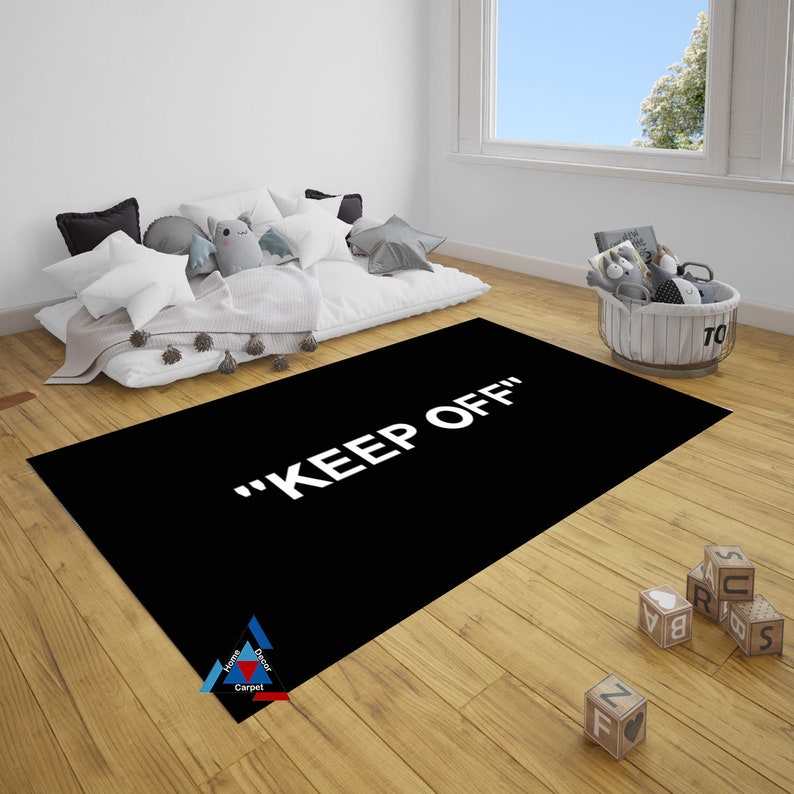 May include: Black and white rug with the text "KEEP OFF" in white letters. The rug is on a wooden floor in a room with a white wall and a window.