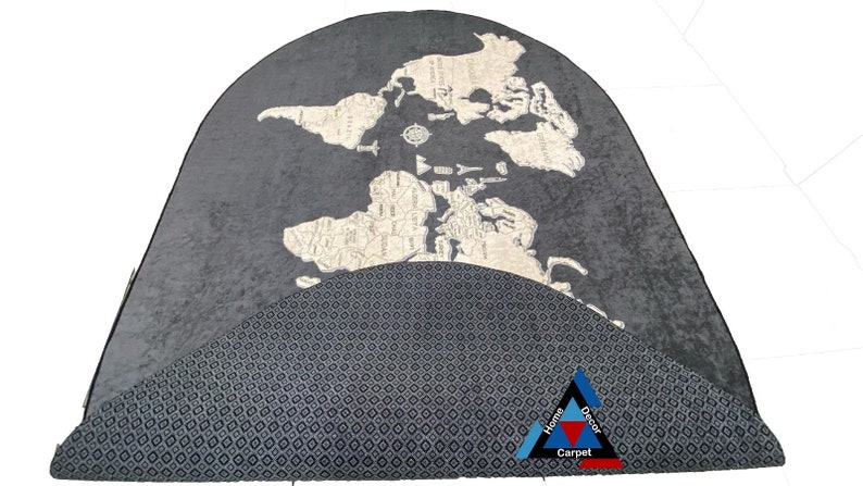 May include: A gray and white world map rug with a black and white geometric pattern on the bottom half. The rug is in the shape of a half circle. The text "Home Decor Carpet" is in the bottom right corner.