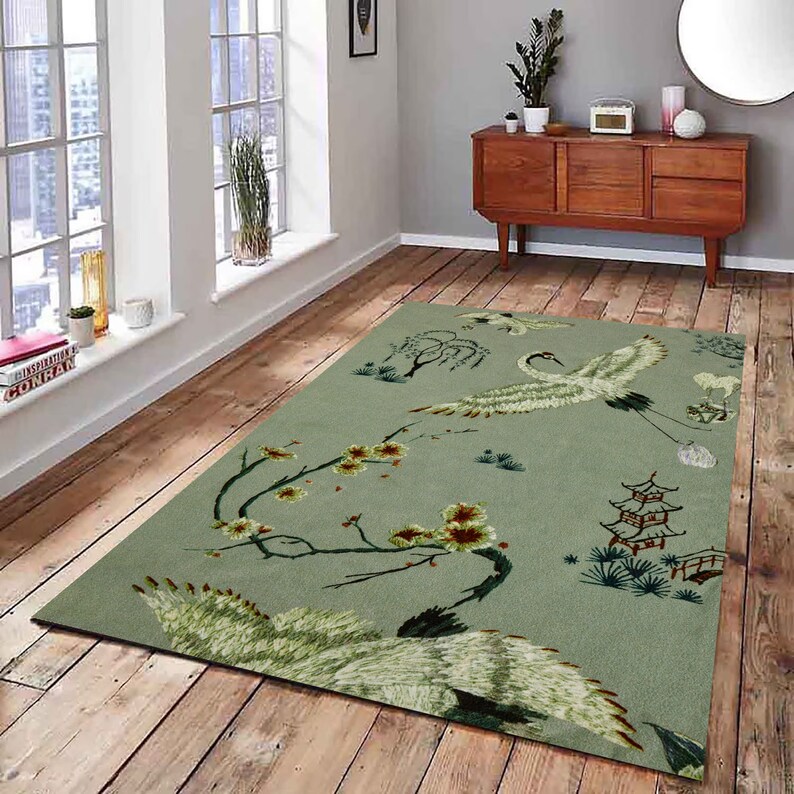 May include: A green area rug with a white crane design, a pagoda, and a bridge. The rug has a floral pattern with pink and brown flowers.