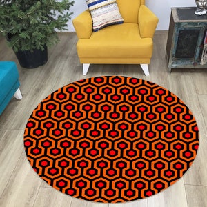 May include: A round rug with a geometric pattern of orange and red hexagons on a black background. The rug is in a living room setting with a yellow armchair and a blue couch.
