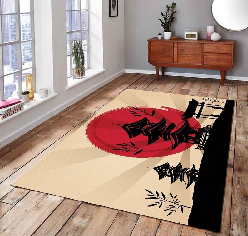 May include: A beige rug with a red sun and black silhouette of a Japanese pagoda and trees. The rug has a graphic design with a sunburst pattern.