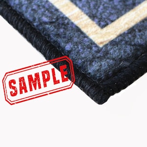 May include: Close-up of a blue and beige patterned rug with black edging. The rug has a "SAMPLE" stamp in red.