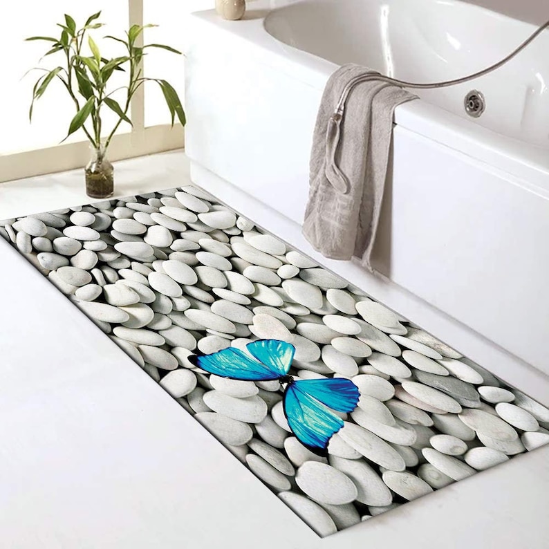 May include: A white bathroom rug with a blue butterfly design on a background of white pebbles.