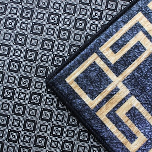May include: Close-up of two different patterned rugs. The top rug has a black background with a white geometric pattern. The bottom rug has a dark blue background with a gold geometric pattern. The word "SAMPLE" is stamped in red on the bottom rug.