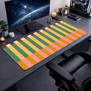 May include: A colorful desk mat with a geometric pattern of vertical stripes in yellow, green, pink, and orange. The mat is rectangular and sits on a dark desk, with a computer monitor and other desk accessories visible in the background.