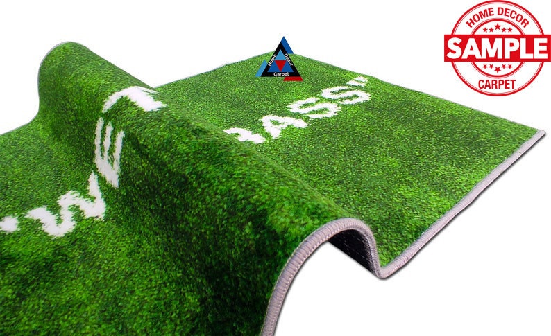 May include: Green artificial grass rug with white text that reads "MASS" on the right side and "WELCOME" on the left side. The rug has a grey border.