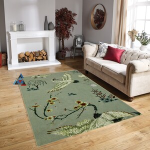 May include: A green and white area rug with a floral design featuring cranes and cherry blossoms. The rug is in a living room setting with a white couch and a fireplace.