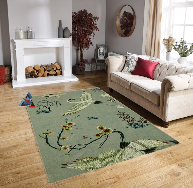 May include: A green and white area rug with a floral design featuring cranes and cherry blossoms. The rug is in a living room setting with a white couch and a fireplace.