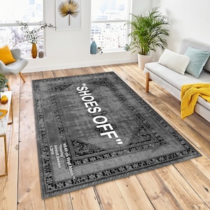 May include: A gray rug with a black and white patterned border. The text "SHOES OFF" is printed in white on the rug. The rug is on a wooden floor.