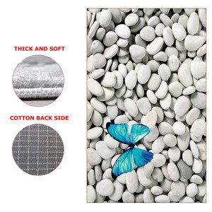 May include: A blue butterfly with white accents sits on a bed of white stones. The stones are smooth and round, and the butterfly is in the centre of the image.