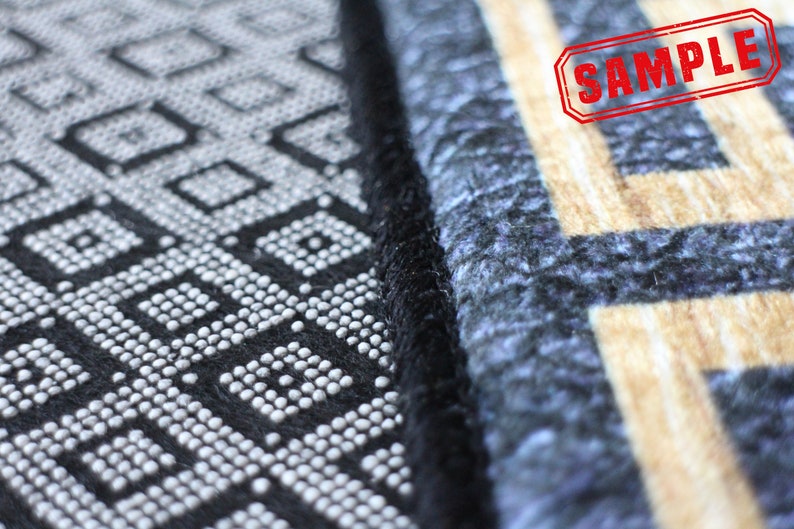 May include: Close-up of a black and white patterned rug with a black border. The rug has a geometric design with small white circles. The rug is next to a blue and beige patterned rug with a black border. The word "SAMPLE" is stamped in red on the blue and beige rug.