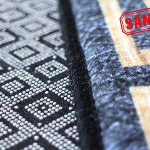 May include: Close-up of a black and white patterned rug with a black border. The rug has a geometric design with small white circles. The rug is next to a blue and beige patterned rug with a black border. The word "SAMPLE" is stamped in red on the beige rug.