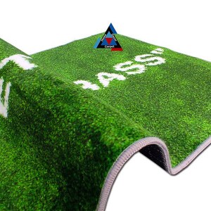 May include: Green artificial grass rug with white text that reads "MASS" on the right side and "WELCOME" on the left side. The rug has a grey border.