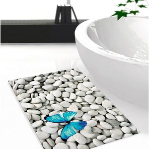 May include: A white bathroom rug with a blue butterfly design. The rug is made to look like a bed of white stones.