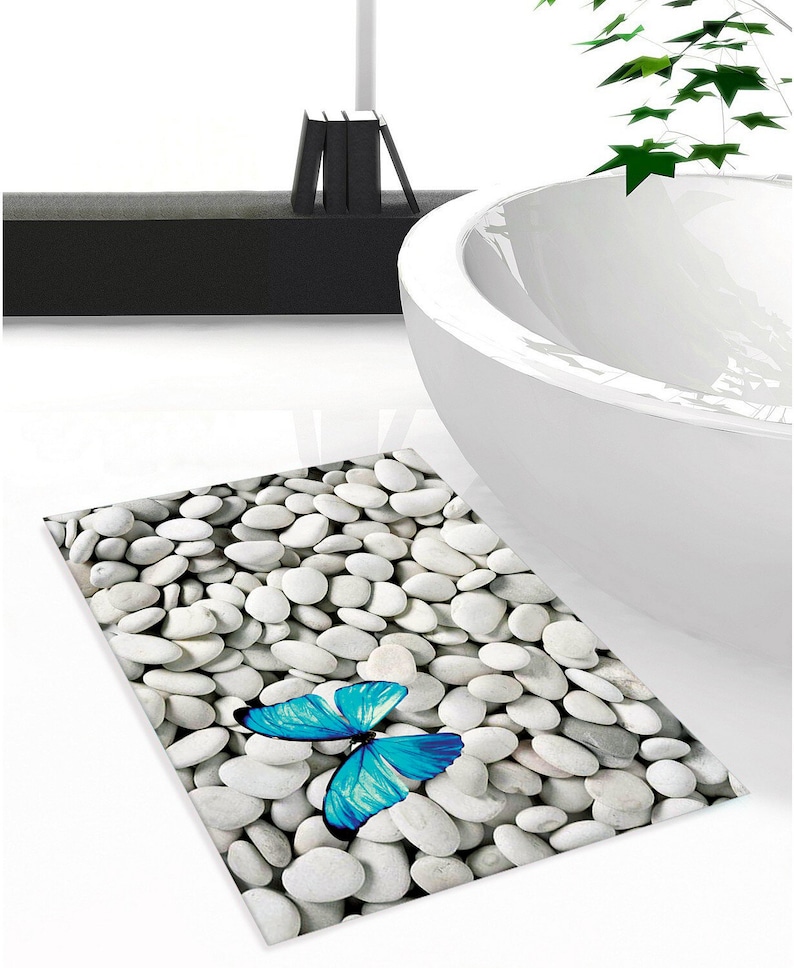 May include: A white bathroom rug with a blue butterfly design. The rug is made to look like a bed of white stones.