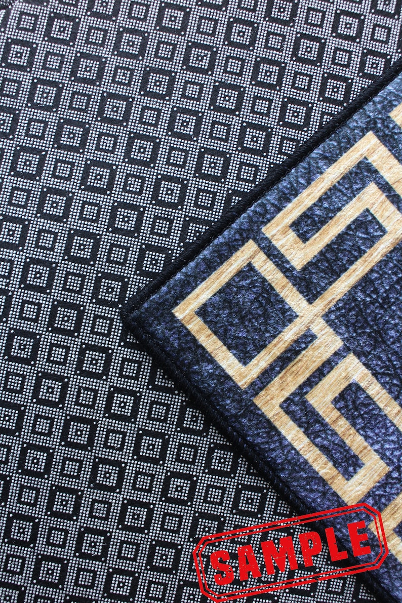 May include: Close-up of two different patterned rugs. The top rug has a black background with a white geometric pattern. The bottom rug has a dark blue background with a gold geometric pattern. The word "SAMPLE" is stamped in red on the bottom rug.