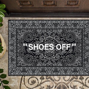 K&ouml;nnte beinhalten: Schwarz-wei&szlig;er Fu&szlig;abtreter mit Paisley-Muster und dem Text "SHOES OFF" in Wei&szlig;.