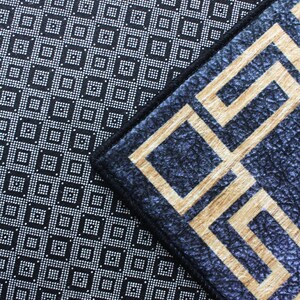 Puede incluir: Una alfombra con un patr&oacute;n geom&eacute;trico en blanco y negro con un borde con un patr&oacute;n geom&eacute;trico azul y dorado. La alfombra tiene un sello "SAMPLE" en rojo.