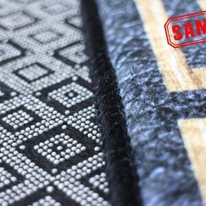Puede incluir: Primer plano de una alfombra de patr&oacute;n blanco y negro con un borde negro. La alfombra tiene un dise&ntilde;o geom&eacute;trico con peque&ntilde;os c&iacute;rculos blancos. La alfombra est&aacute; junto a una alfombra de patr&oacute;n azul y beige con un borde negro. La palabra "SAMPLE" est&aacute; estampada en rojo en la alfombra beige.