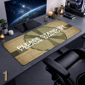 Puede incluir: Alfombrilla de escritorio rectangular con un diseño de patrón de prueba de televisión retro. La alfombrilla es principalmente de color beige con un gran gráfico circular verde y las palabras "PLEASE STAND BY" en blanco. Se ve un monitor de computadora y otros accesorios de escritorio.