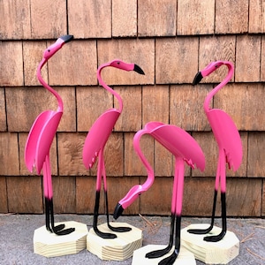 Puede incluir: Cuatro decoraciones de jardín de flamencos rosas hechas de metal reciclado. Cada flamenco está de pie sobre una base de madera.