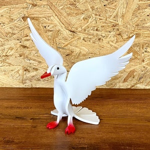 May include: White wooden dove with red accents, standing on a wooden surface. The dove has its wings spread out.