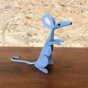 May include: A gray metal mouse figurine with pink ears and black eyes. The mouse is standing on a wooden surface.