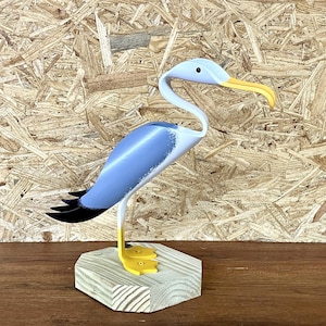 May include: A wooden bird sculpture with a gray body, black wings, and yellow beak and feet. The bird is standing on a wooden base.