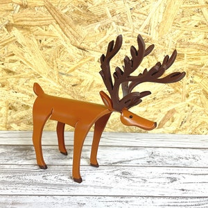 May include: A wooden reindeer figurine with brown antlers and a brown body. The reindeer is standing on a white wooden surface.