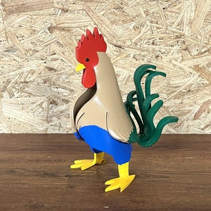 May include: A colorful metal rooster figurine with a red comb, brown body, blue wings, and green tail feathers. The rooster is standing on a wooden surface.