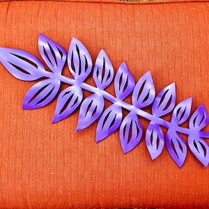 May include: Purple metal leaf branch with a cutout design. The branch is on a textured orange background.