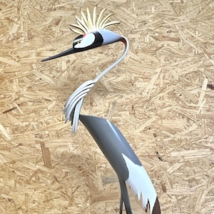 May include: A gray and white wooden sculpture of a crane with a gold head and beak. The crane is standing on a wooden surface.