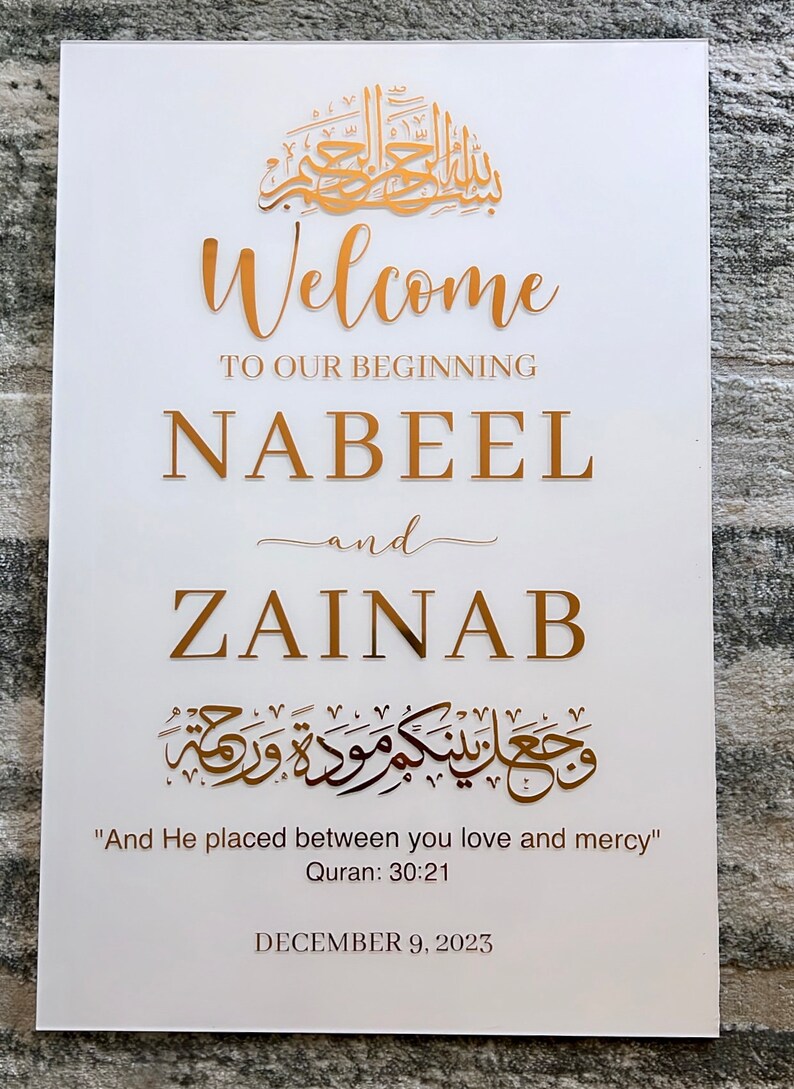 May include: A white rectangular sign featuring gold lettering that reads Welcome to our beginning, Nabeel and Zainab, along with Arabic calligraphy, the English translation And He placed between you love and mercy, Quran 30:21, and December 9, 2023.