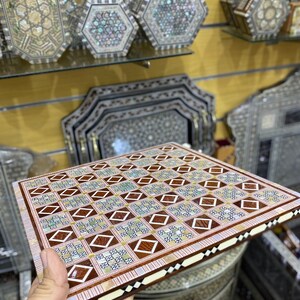 May include: A wooden backgammon board inlaid with mother of pearl and intricate geometric patterns. The board is brown and white with a red and white border.
