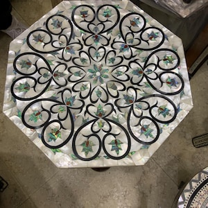 Könnte beinhalten: Achteckiger Tischplatte mit einer dekorativen Einlage aus Perlmutt und schwarzem Holz. Das Design zeigt ein sich wiederholendes Muster aus Herzen und Blumen.