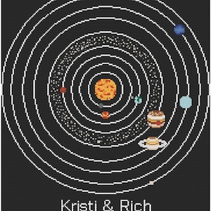 May include: A cross-stitch representation of the solar system, with the sun at the centre and planets and rings. The names "Kristi & Rich" and the date "09-05-2021" are stitched at the bottom, set against a black backdrop.