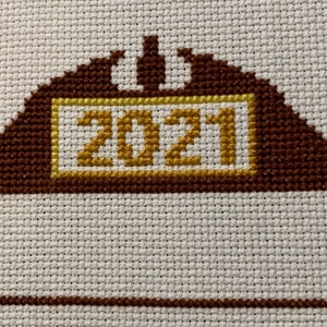 May include: A brown and gold cross-stitch design with the year 2021 in the centre.