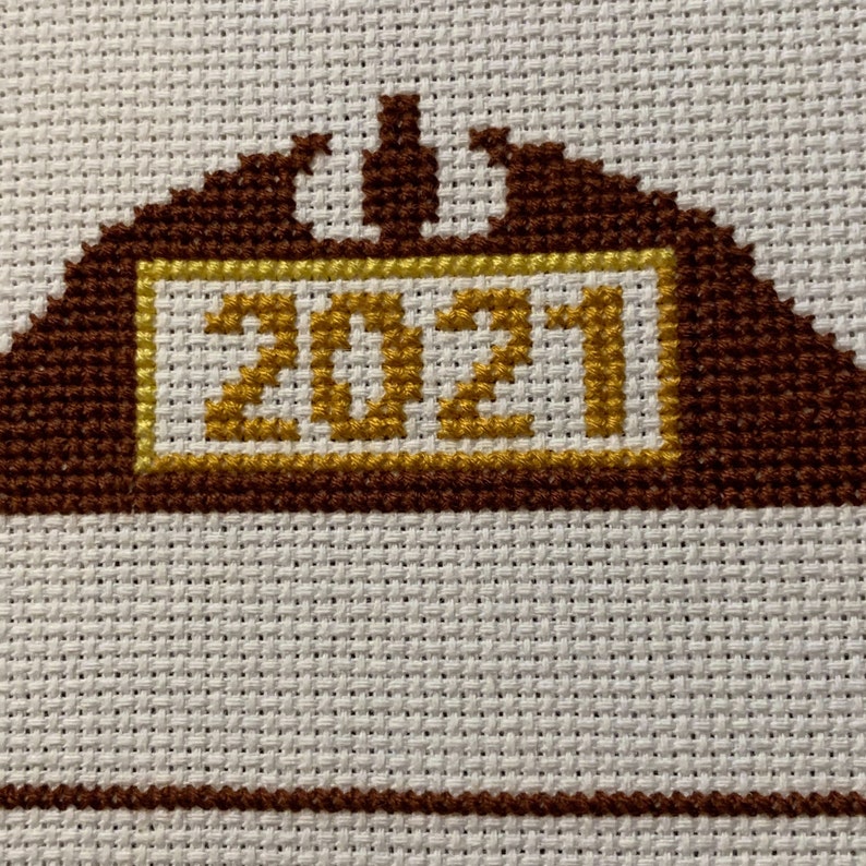 May include: A brown and gold cross-stitch design with the year 2021 in the centre.