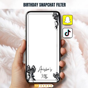 Può includere: Uno schermo di smartphone mostra un filtro Snapchat di compleanno. Il filtro ha uno sfondo bianco con fiocchi neri e il testo "Anisha's 30th". I loghi di Snapchat e TikTok sono visibili. Il telefono è tenuto in mano.