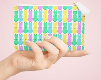 Op de afbeelding: Een witte ritszak met een herhalend patroon van pastelgele, blauwe, groene en roze konijnvormige snoepjes.